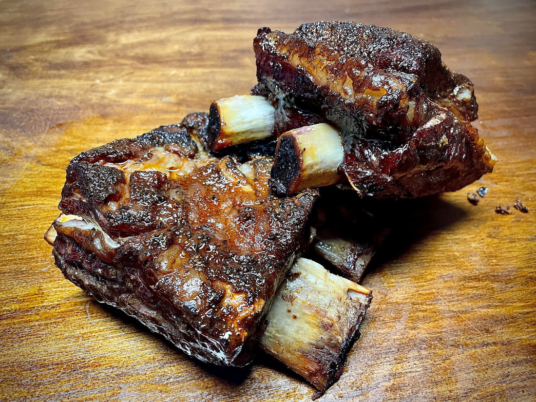 A rack of slow-smoked beef short ribs seasoned with Holy Smokers Holy Heifer rub, showing a dark bark crust, rendered fat, and juicy marbling, with a tender, melt-in-your-mouth texture and rich BBQ smoke flavor.