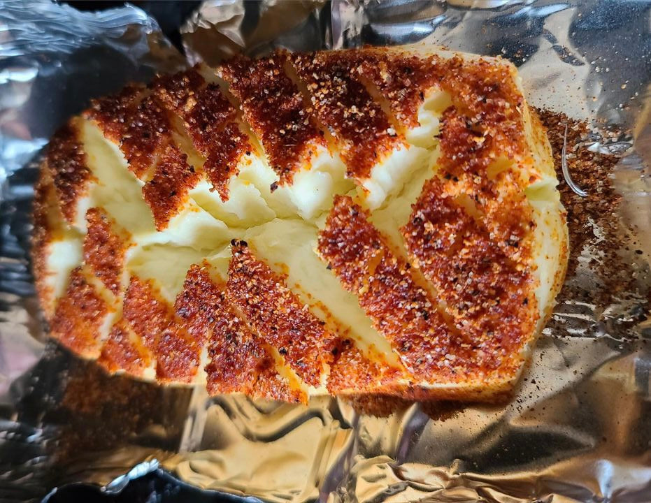 A block of smoked cream cheese coated in a honey pecan seasoning and wrapped in crispy bacon, showing a caramelized, golden-brown crust with a creamy center, presented as a rich, smoky appetizer.