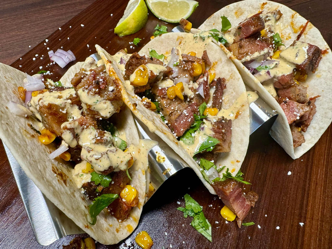 Smoked brisket street corn tacos with tender shredded brisket, roasted corn, and cotija cheese in charred tortillas, topped with chili lime sauce, cilantro, red onions, and lime, showing bold smoky BBQ tacos with citrus-spice flavor.