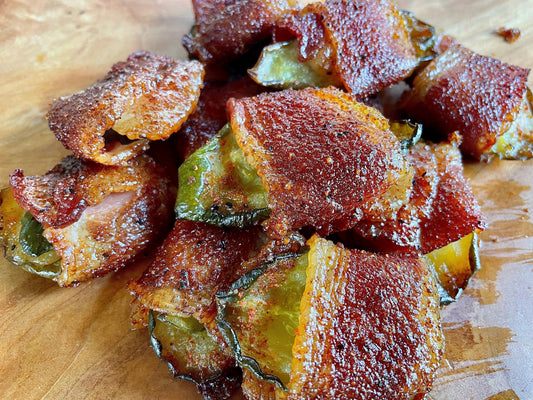 Smoked bacon-wrapped pickles seasoned with savory BBQ rub, showing crispy rendered bacon edges wrapped around pickles, served as a smoky appetizer with a rich, golden-brown finish.