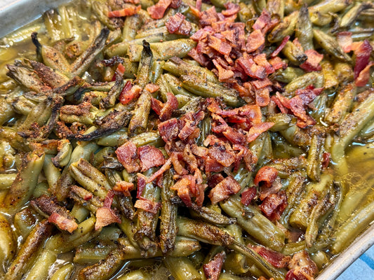 Smoked green beans cooked with crispy bacon and buttery hot sauce, showing a glossy, caramelized finish with visible bacon pieces and a light smoky haze, presented as a bold pecan wood–smoked BBQ side dish.