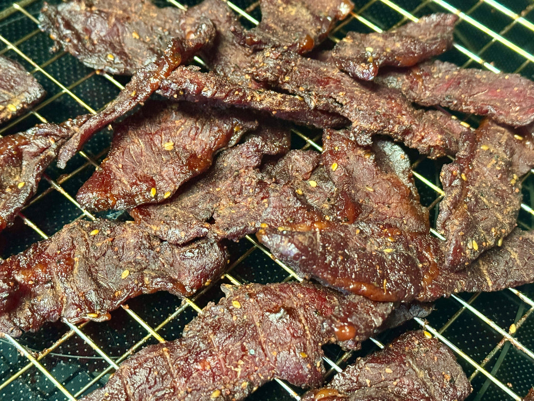 Strips of Holy Smokers Holy Heifer beef jerky made from lean bottom round, slow-smoked over pecan wood, showing a rich dark glaze and seasoned surface, highlighting a bold, smoky, and savory handcrafted jerky texture.