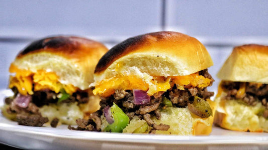 Philly cheesesteak sliders featuring tender sliced steak and melted cheese stuffed into small toasted slider buns, showing gooey, savory beef sliders with rich, melty texture and a golden-brown finish.