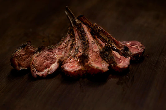 Herb-crusted rack of lamb cooked to tender perfection, showing a juicy, lightly seared exterior with a seasoned herb coating and rich pink interior, presented as a premium 2 lb bone-in protein cut.