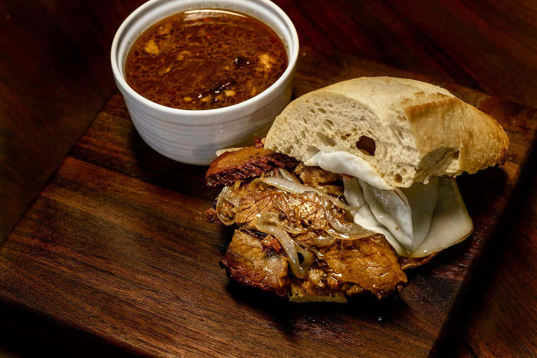 Smoked brisket French dip sandwich with tender sliced beef seasoned with BBQ rub, stacked on a toasted roll and served with a side of rich au jus for dipping, showing a juicy, smoky, and savory sandwich presentation.