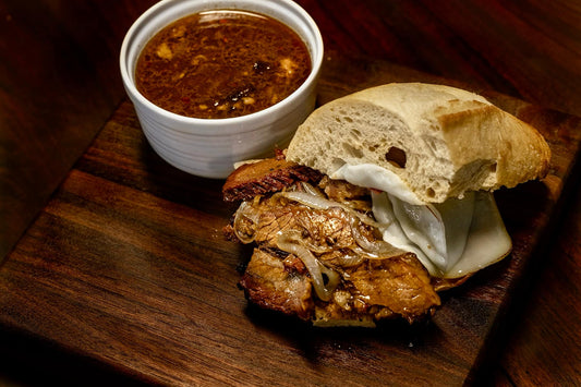 Smoked brisket French dip sandwich with tender sliced beef seasoned with BBQ rub, stacked on a toasted roll and served with a side of rich au jus for dipping, showing a juicy, smoky, and savory sandwich presentation.