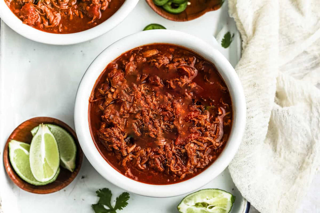 Smoked pulled pork chili featuring tender shredded pork, beans, tomatoes, onions, and spices, shown in a rich, hearty bowl with a thick smoky-red chili base and bold BBQ flavor profile.